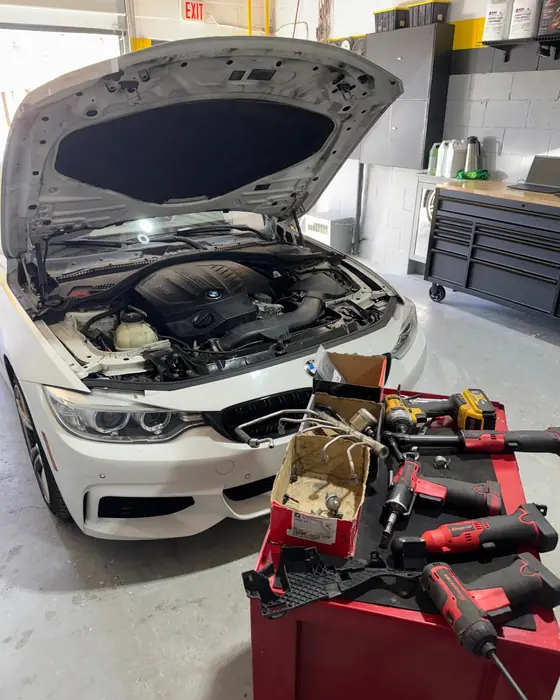 A white BMW with the hood open beside a cart of tools in the GTS Auto Repair bay