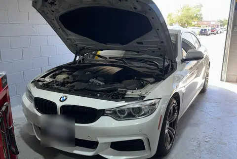 A white BMW with the hood open in the GTS Auto Repair bay